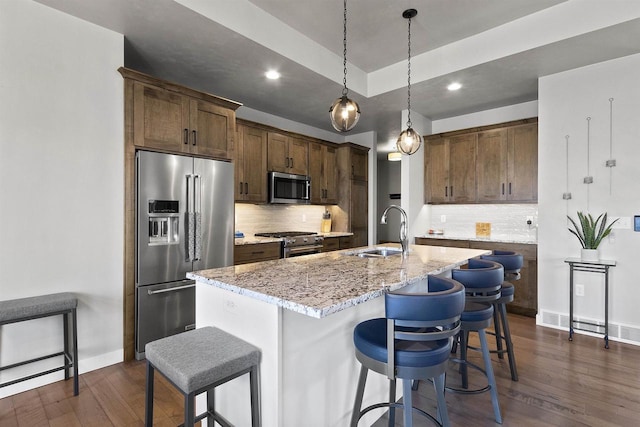 kitchen with a breakfast bar, a sink, premium appliances, dark wood-style floors, and light stone countertops