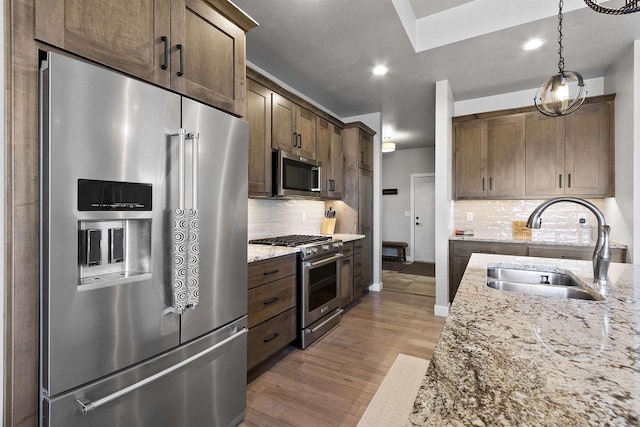 kitchen featuring light wood finished floors, premium appliances, light stone countertops, and a sink