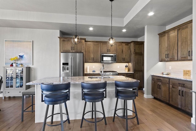 kitchen with dark wood-style floors, stainless steel appliances, a kitchen island with sink, and a sink