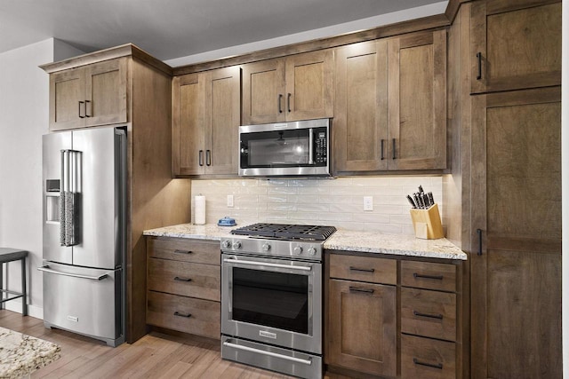 kitchen with stainless steel appliances, light stone countertops, decorative backsplash, and light wood finished floors