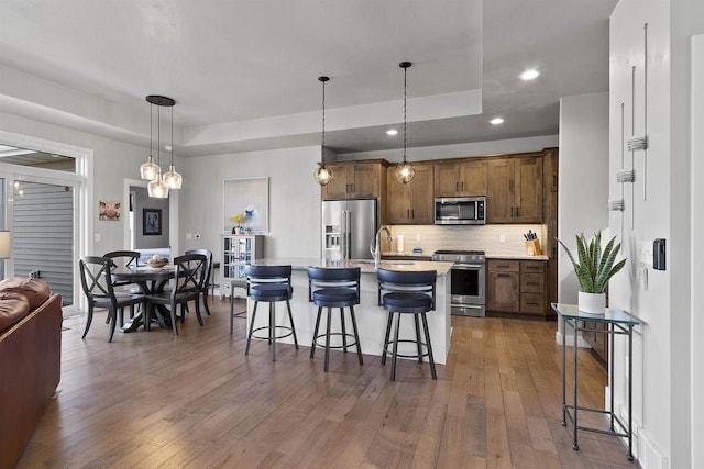 kitchen with a tray ceiling, stainless steel appliances, a kitchen breakfast bar, and hardwood / wood-style floors