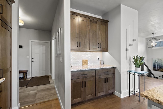 kitchen featuring light stone counters, decorative backsplash, a notable chandelier, and wood finished floors