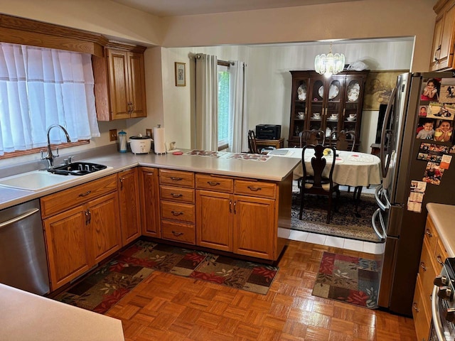 kitchen featuring brown cabinets, a notable chandelier, a sink, appliances with stainless steel finishes, and a peninsula