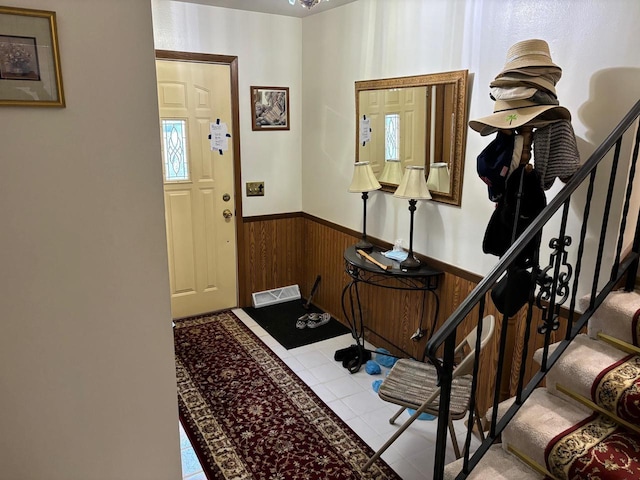 foyer featuring tile patterned flooring, wooden walls, visible vents, stairs, and wainscoting