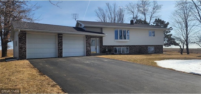 tri-level home with aphalt driveway, an attached garage, brick siding, and a front yard