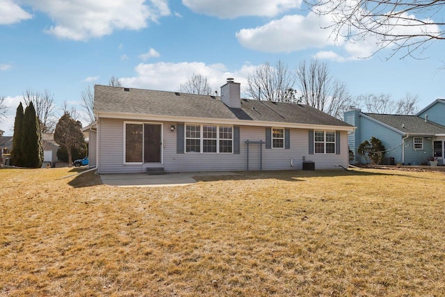 rear view of house featuring a shingled roof, a patio, a yard, and a chimney