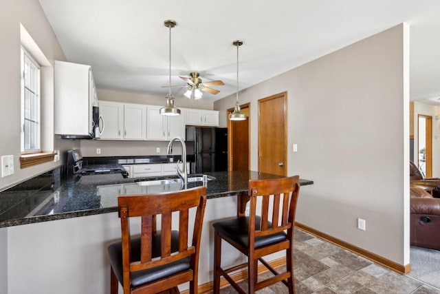 kitchen with gas range, a peninsula, freestanding refrigerator, hanging light fixtures, and a sink