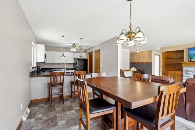 dining area with a brick fireplace, built in shelves, stone finish flooring, baseboards, and a chandelier