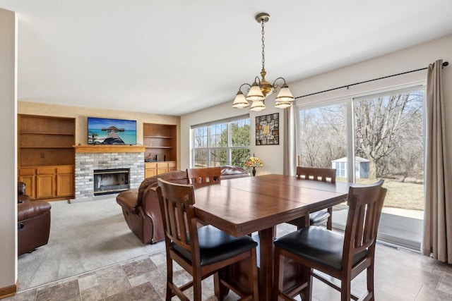 dining space with visible vents, a brick fireplace, built in features, light colored carpet, and an inviting chandelier