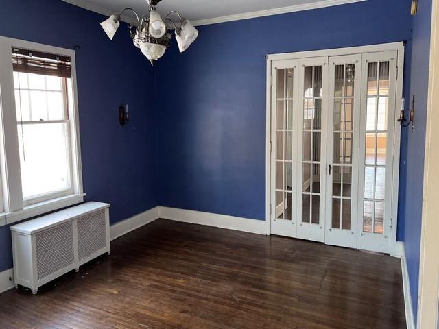 spare room featuring radiator, baseboards, ornamental molding, wood finished floors, and a notable chandelier