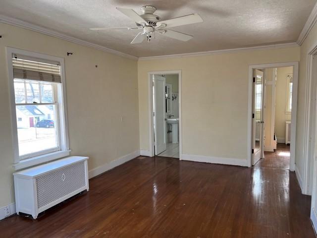 empty room with wood finished floors, radiator heating unit, and crown molding