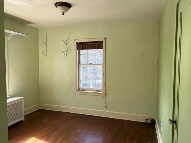 empty room featuring radiator, dark wood-style floors, and baseboards