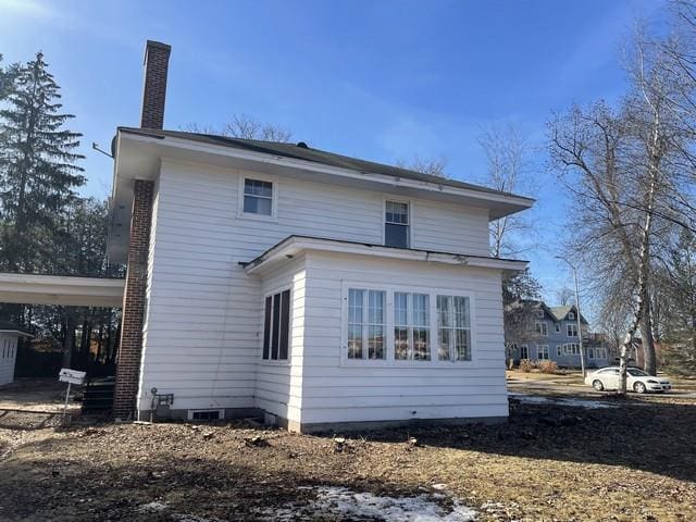 back of house featuring an attached carport and a chimney