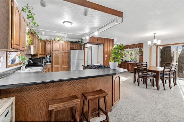 kitchen with brown cabinets, a sink, freestanding refrigerator, a peninsula, and light colored carpet