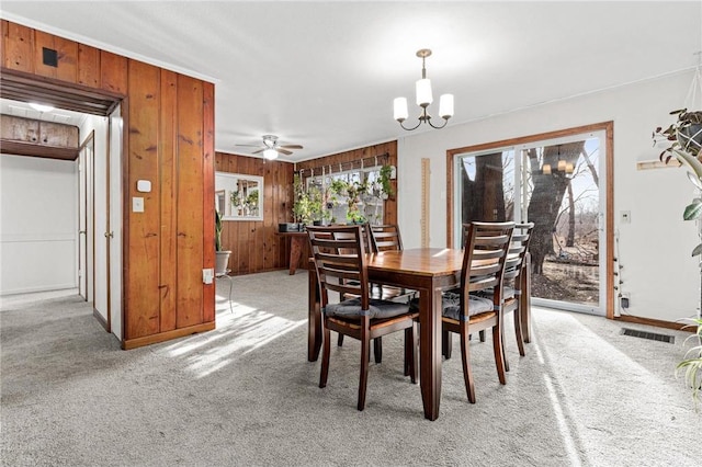 dining space with wooden walls, light colored carpet, baseboards, and an inviting chandelier