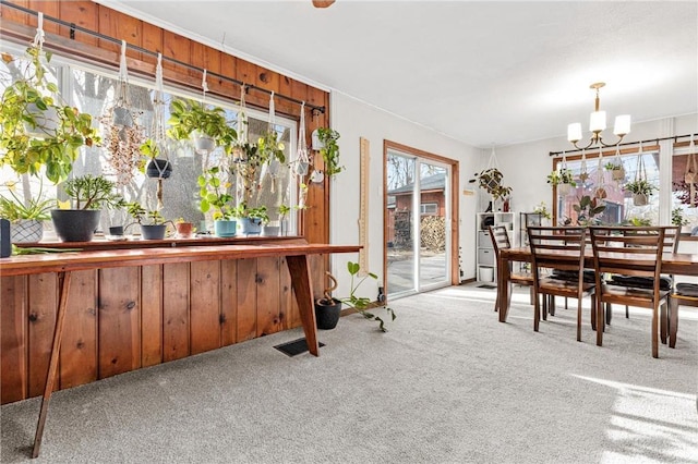 dining space with wooden walls, a notable chandelier, visible vents, and carpet