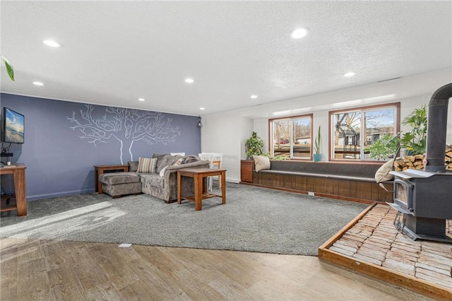 living area with recessed lighting, a textured ceiling, wood finished floors, and a wood stove