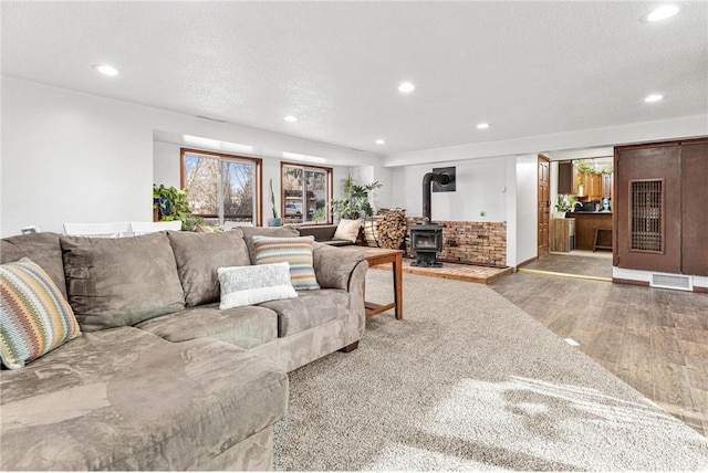 living room with a wood stove, recessed lighting, wood finished floors, and a textured ceiling