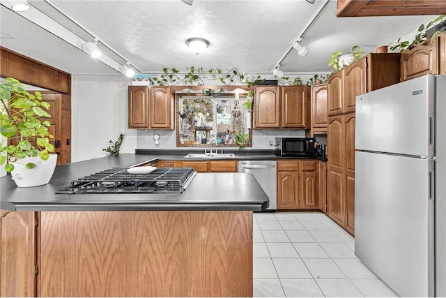 kitchen with dark countertops, backsplash, light tile patterned floors, brown cabinets, and stainless steel appliances