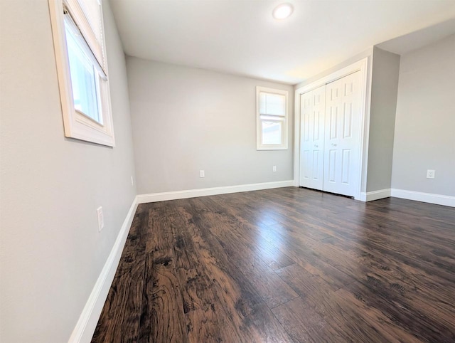 unfurnished bedroom featuring a closet, dark wood-type flooring, and baseboards