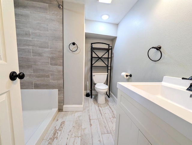 bathroom with toilet, wood finished floors, tiled shower, baseboards, and vanity