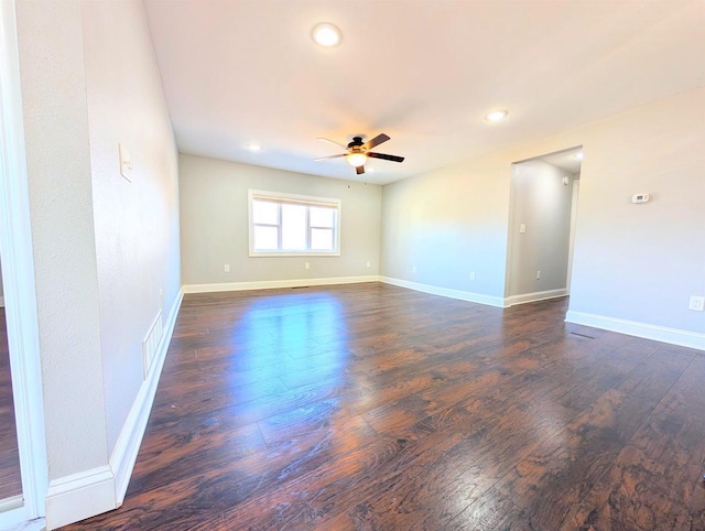 unfurnished room with a ceiling fan, visible vents, dark wood-style floors, and baseboards