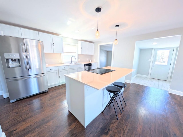 kitchen with a sink, dark wood finished floors, appliances with stainless steel finishes, white cabinets, and hanging light fixtures