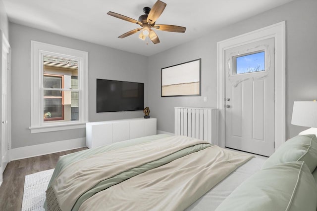 bedroom with a ceiling fan, radiator heating unit, baseboards, and wood finished floors