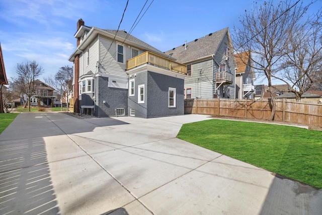 back of house with a yard, a balcony, a chimney, and fence