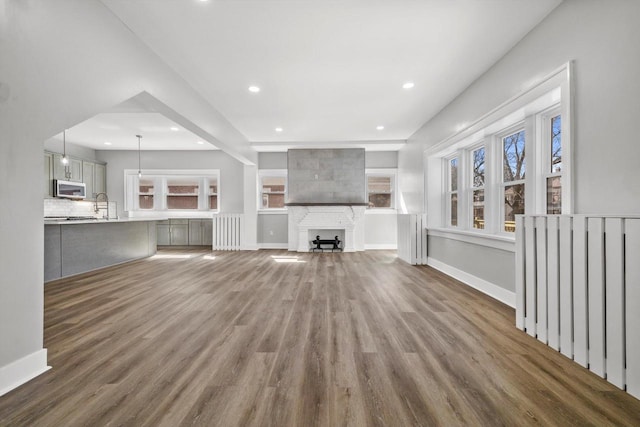 unfurnished living room featuring recessed lighting, a large fireplace, baseboards, and wood finished floors