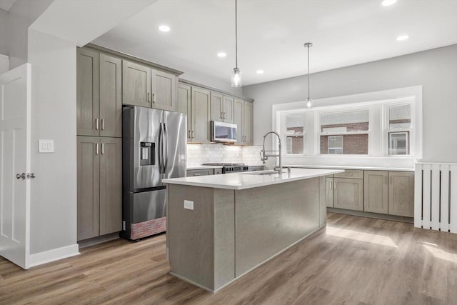 kitchen featuring a center island with sink, a sink, tasteful backsplash, light wood-style floors, and appliances with stainless steel finishes