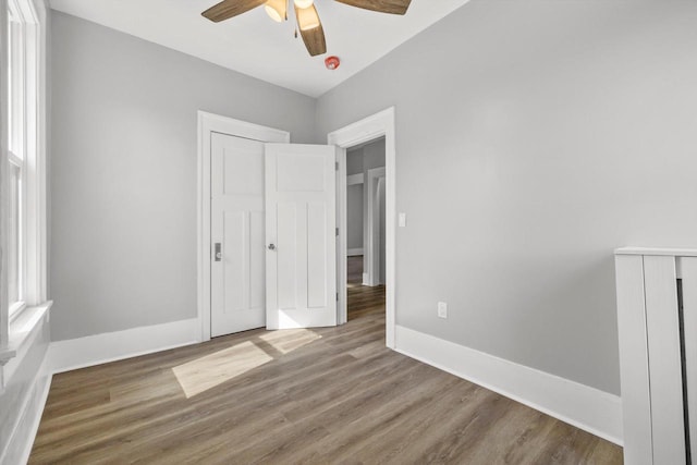 unfurnished bedroom featuring a ceiling fan, wood finished floors, baseboards, and a closet