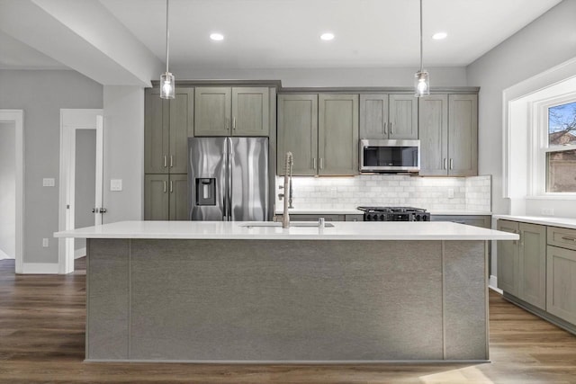 kitchen with a center island with sink, a sink, stainless steel appliances, light countertops, and backsplash