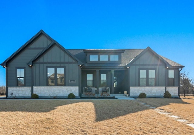 back of property with a yard, board and batten siding, stone siding, and roof with shingles