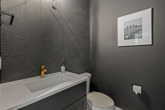 bathroom with toilet, vanity, and a textured wall