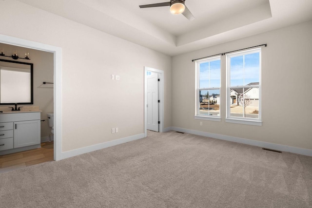 unfurnished bedroom with visible vents, baseboards, a tray ceiling, a sink, and light carpet