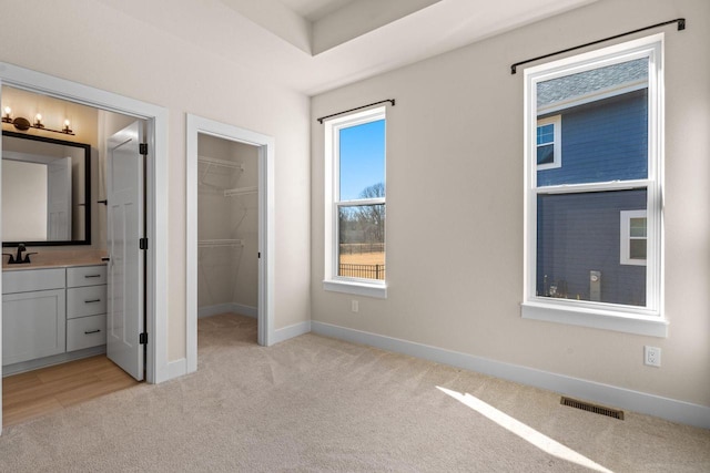 unfurnished bedroom with visible vents, a walk in closet, baseboards, light carpet, and a sink