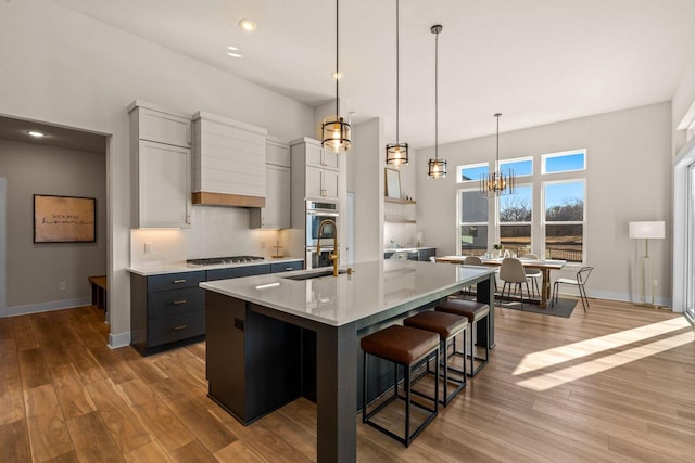 kitchen with wood finished floors, a kitchen island with sink, a sink, stainless steel appliances, and light countertops