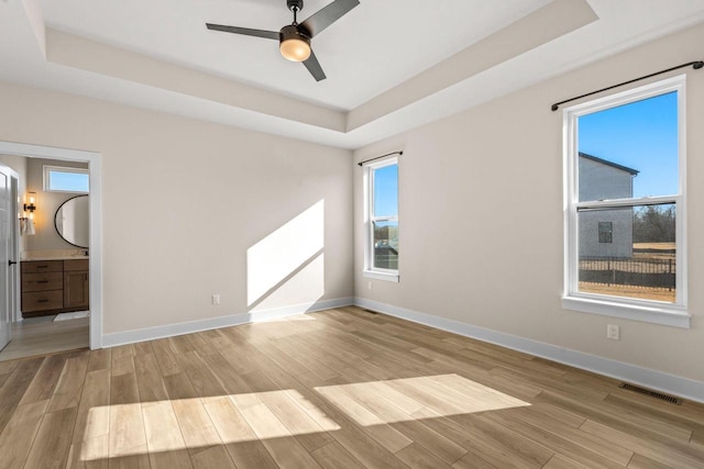 unfurnished bedroom with light wood finished floors, visible vents, baseboards, and a tray ceiling