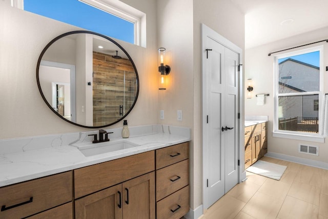 bathroom with vanity, baseboards, visible vents, and a tile shower