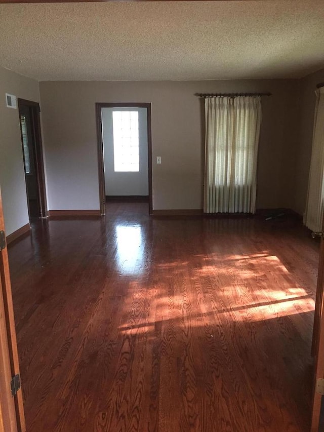 spare room featuring visible vents, a textured ceiling, baseboards, and wood finished floors