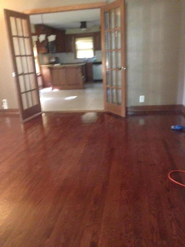 unfurnished living room with french doors, baseboards, and wood finished floors