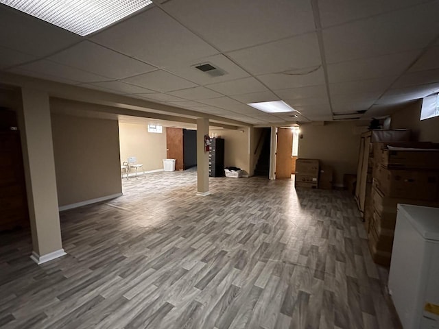 finished basement with visible vents, a paneled ceiling, baseboards, and wood finished floors