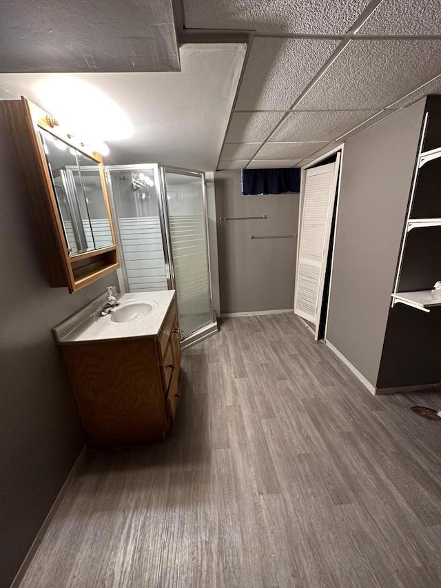 bathroom featuring a shower stall, baseboards, wood finished floors, vanity, and a paneled ceiling