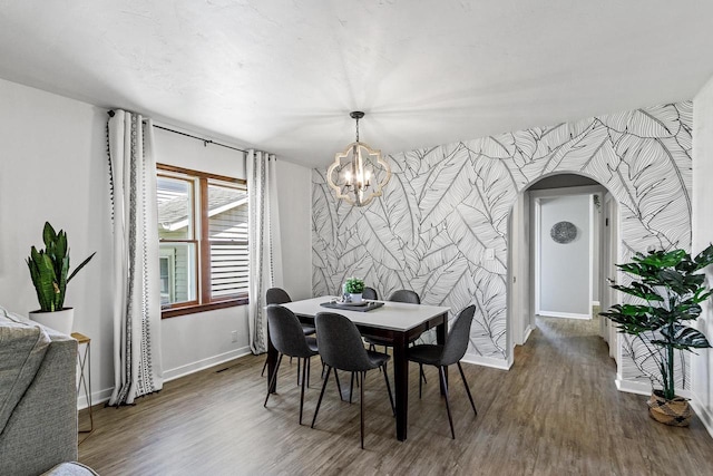 dining room featuring wallpapered walls, dark wood-type flooring, baseboards, a chandelier, and arched walkways