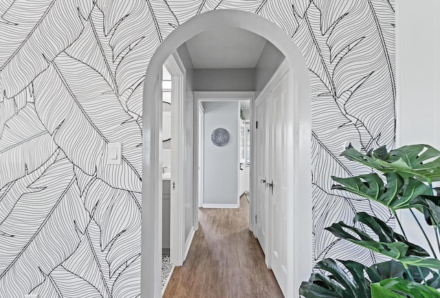 corridor featuring arched walkways, baseboards, and wood finished floors