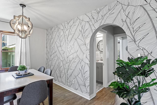 dining area featuring wood finished floors, baseboards, an inviting chandelier, arched walkways, and an accent wall