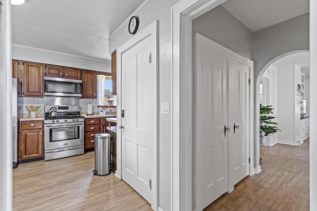 kitchen featuring arched walkways, light wood-style floors, appliances with stainless steel finishes, and light countertops