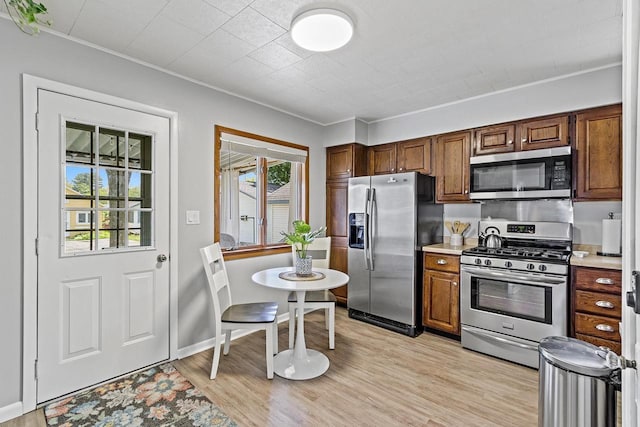 kitchen with baseboards, ornamental molding, light countertops, appliances with stainless steel finishes, and light wood-type flooring