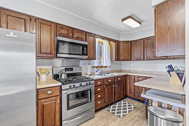 kitchen with light wood finished floors, a sink, appliances with stainless steel finishes, crown molding, and light countertops